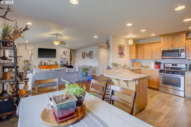 kitchen with a kitchen breakfast bar, kitchen peninsula, sink, appliances with stainless steel finishes, and light brown cabinetry