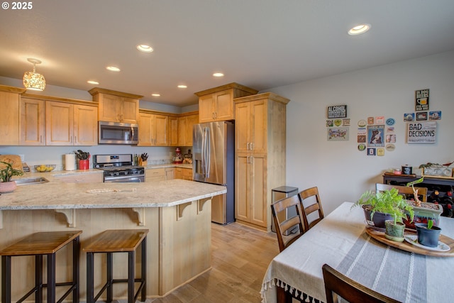 kitchen featuring appliances with stainless steel finishes, light stone countertops, light brown cabinets, light wood-type flooring, and kitchen peninsula