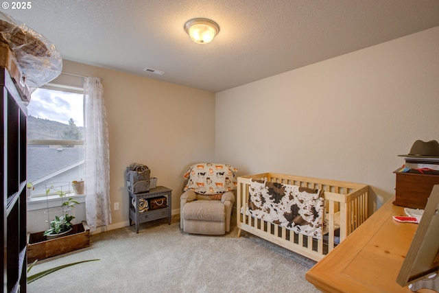 bedroom with a crib, carpet floors, and a textured ceiling