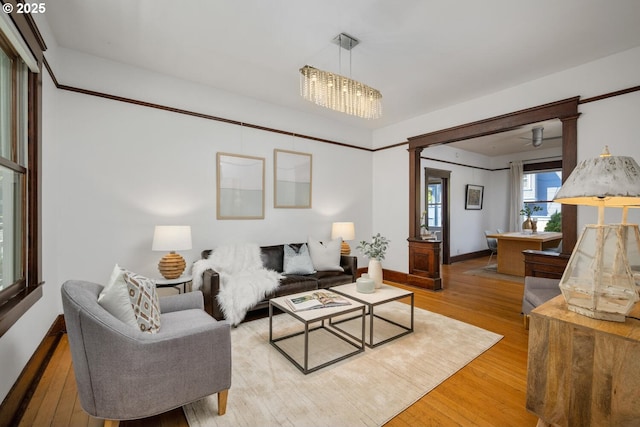 living room featuring light wood finished floors, decorative columns, a chandelier, and baseboards
