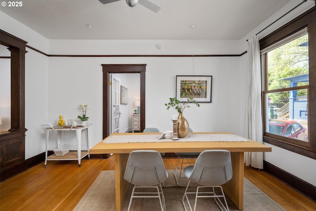 dining area featuring wood finished floors, ceiling fan, baseboards, and ornate columns