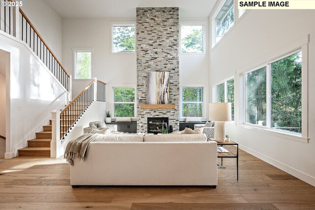living room featuring stairs, a stone fireplace, plenty of natural light, and wood finished floors
