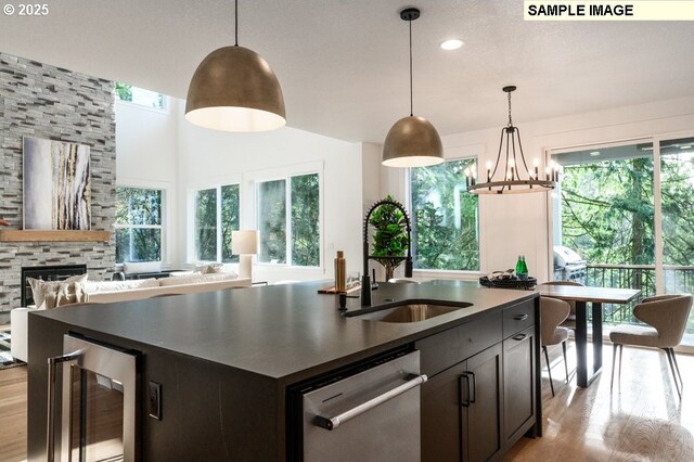 kitchen featuring dark countertops, a sink, dishwasher, an island with sink, and wine cooler