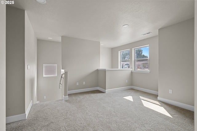 carpeted spare room featuring visible vents, a textured ceiling, and baseboards