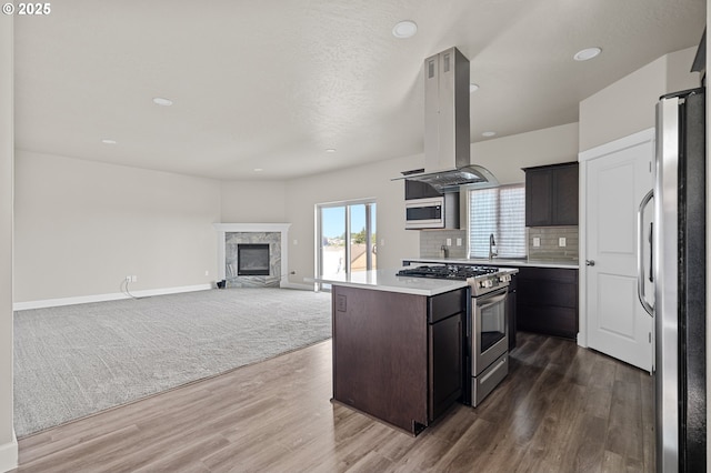 kitchen with dark wood-style flooring, dark brown cabinetry, island range hood, light countertops, and appliances with stainless steel finishes