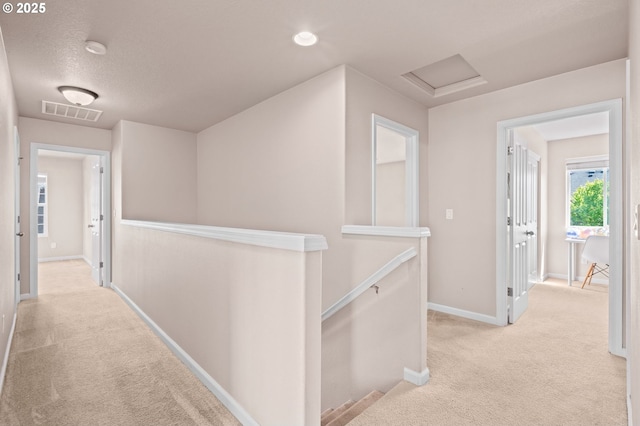 corridor with an upstairs landing, carpet flooring, baseboards, and attic access
