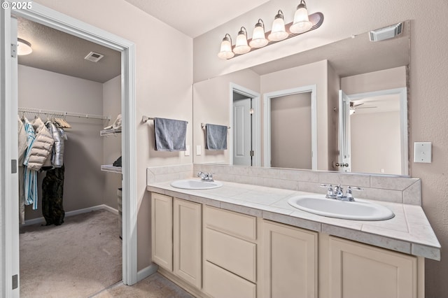 bathroom with double vanity, a walk in closet, ceiling fan, and baseboards