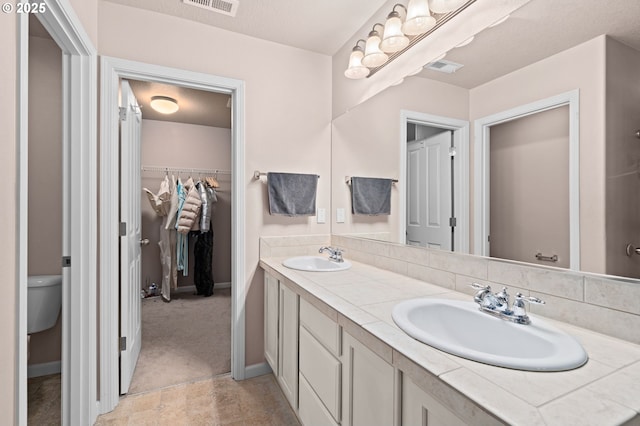 full bathroom with toilet, a spacious closet, double vanity, and baseboards