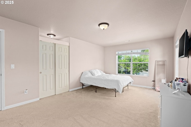 bedroom featuring light colored carpet, baseboards, and a closet