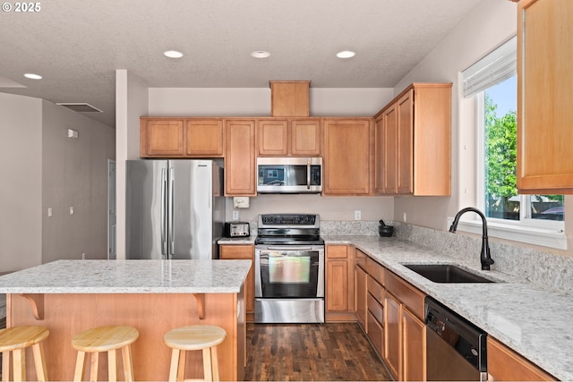 kitchen with stainless steel appliances, a sink, dark wood-style floors, a kitchen bar, and a kitchen island