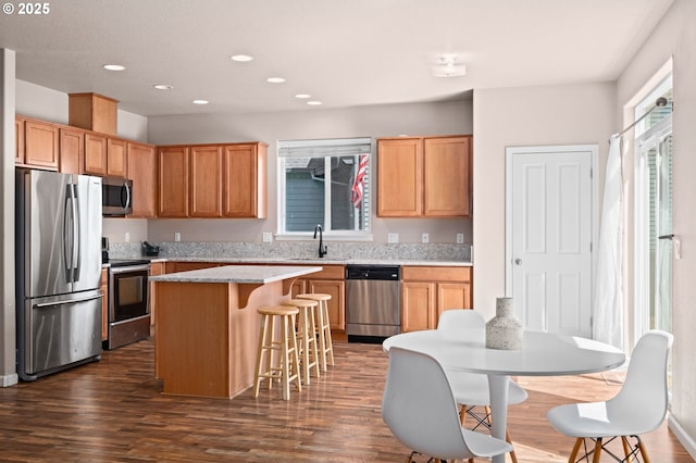 kitchen featuring appliances with stainless steel finishes, a sink, a center island, a kitchen bar, and dark wood-style flooring