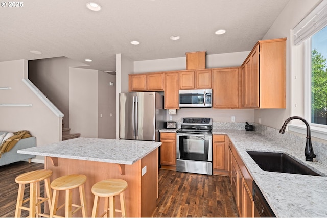 kitchen with appliances with stainless steel finishes, a sink, dark wood finished floors, a kitchen island, and light stone countertops