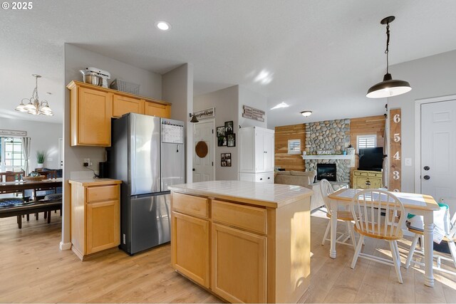 kitchen featuring light brown cabinets, freestanding refrigerator, a stone fireplace, tile counters, and light wood-type flooring