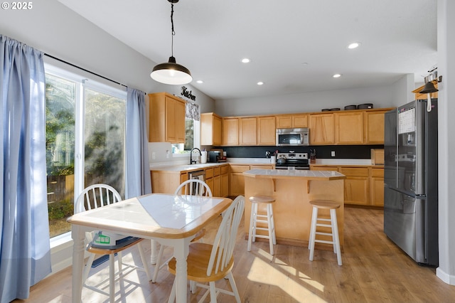 kitchen featuring light wood finished floors, a kitchen island, a sink, light countertops, and appliances with stainless steel finishes