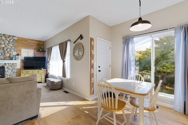 dining space with light wood-type flooring, baseboards, wood walls, and a fireplace