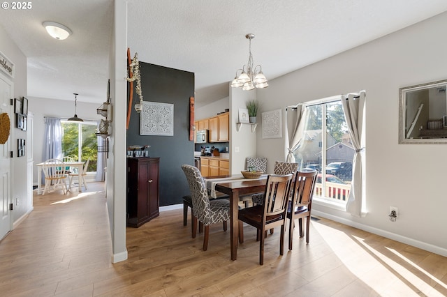 dining space featuring a textured ceiling, light wood-style floors, baseboards, and a chandelier