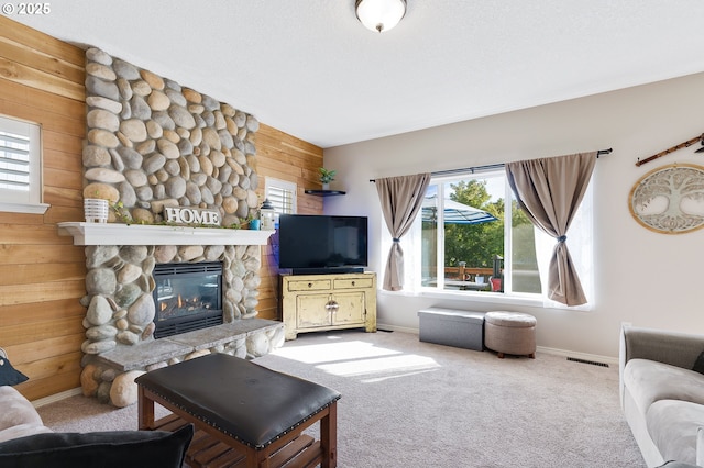 carpeted living area featuring wooden walls, visible vents, baseboards, a fireplace, and a textured ceiling