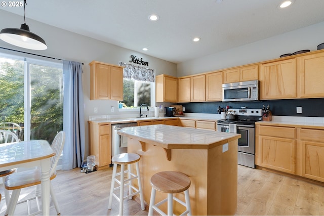 kitchen with tile counters, light wood-style flooring, appliances with stainless steel finishes, and light brown cabinetry