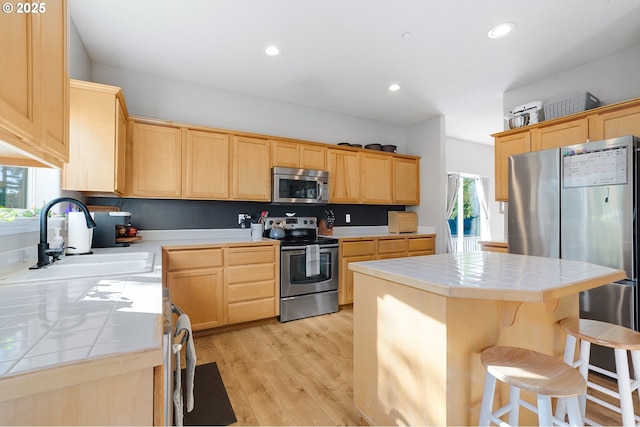 kitchen featuring light brown cabinetry, tile countertops, appliances with stainless steel finishes, and a sink