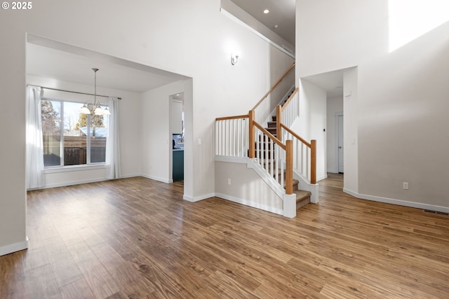 unfurnished living room featuring a towering ceiling, a chandelier, and light hardwood / wood-style floors