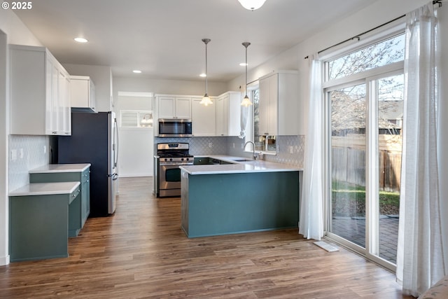 kitchen featuring appliances with stainless steel finishes, pendant lighting, hardwood / wood-style flooring, sink, and white cabinetry