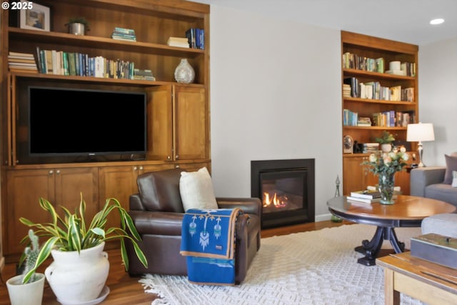 sitting room with a glass covered fireplace, built in shelves, recessed lighting, and wood finished floors
