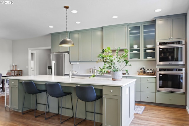 kitchen with light wood-style floors, an island with sink, recessed lighting, a sink, and stainless steel appliances