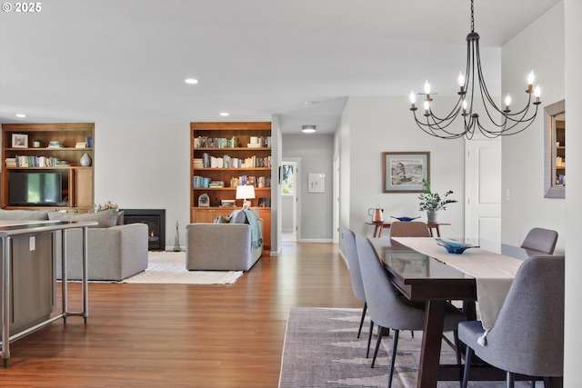 dining room with a notable chandelier, a glass covered fireplace, built in features, recessed lighting, and wood finished floors
