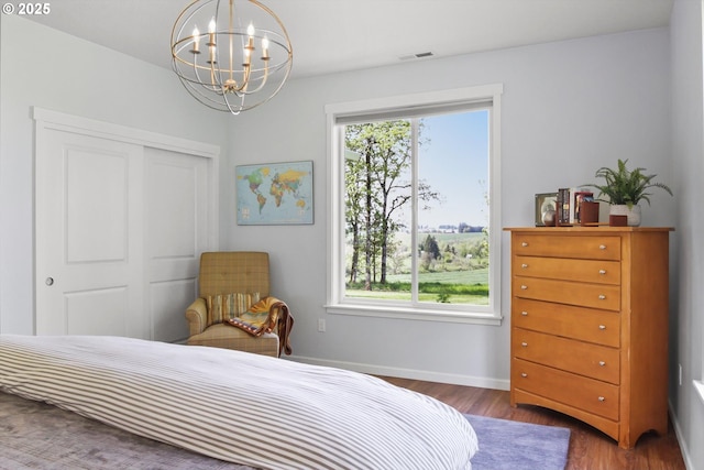 bedroom with visible vents, a closet, an inviting chandelier, wood finished floors, and baseboards
