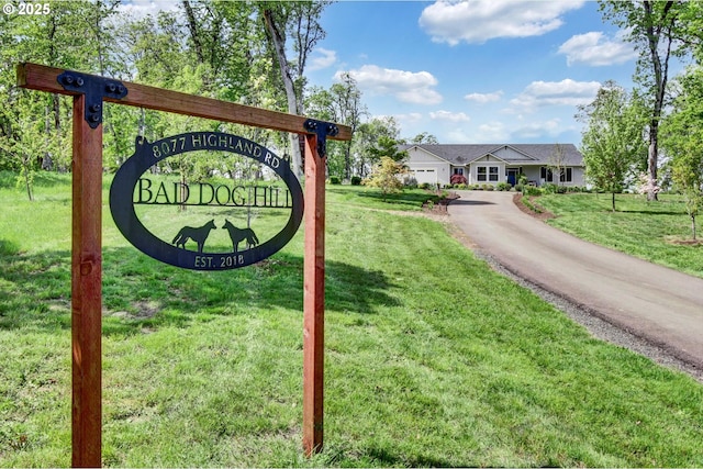 community / neighborhood sign with a lawn, a garage, and aphalt driveway