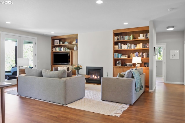 living room with recessed lighting, a glass covered fireplace, built in features, and wood finished floors