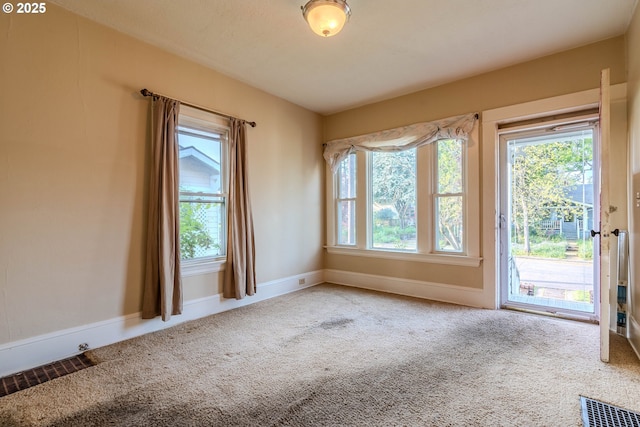carpeted spare room with a healthy amount of sunlight, baseboards, and visible vents