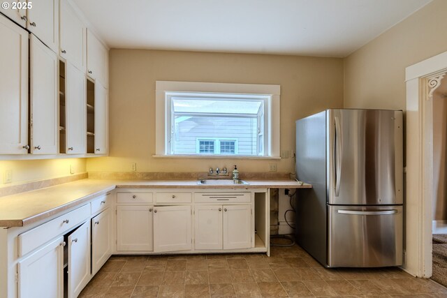 kitchen with a sink, light countertops, freestanding refrigerator, and white cabinetry