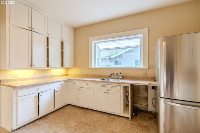 kitchen featuring freestanding refrigerator, a sink, and white cabinetry