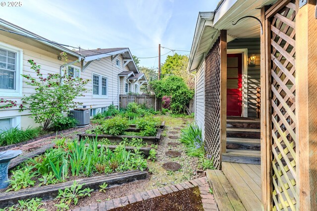 view of yard featuring fence, a garden, central AC unit, and entry steps