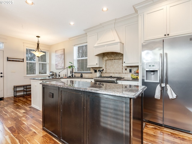 kitchen featuring stainless steel fridge, white cabinetry, hanging light fixtures, a center island, and exhaust hood