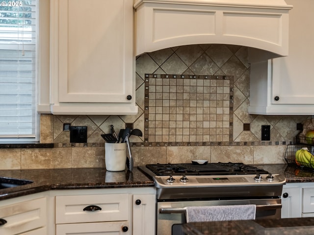 kitchen with dark stone counters, stainless steel gas range, custom range hood, and white cabinets