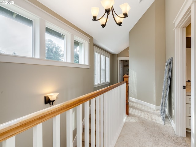 hall featuring vaulted ceiling, light colored carpet, and a notable chandelier