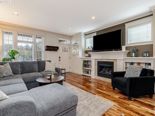 living room featuring a tile fireplace, crown molding, a healthy amount of sunlight, and light wood-type flooring