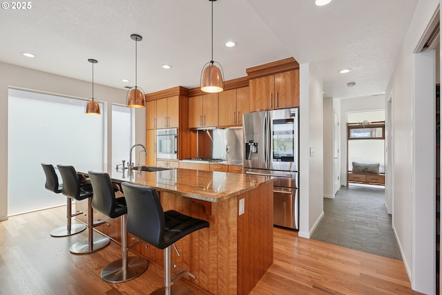 14569 NW Larson Rd Unit 13, Portland, OR 97231 - kitchen with appliances with stainless steel finishes, brown cabinets, light wood finished floors, recessed lighting, and an island with sink