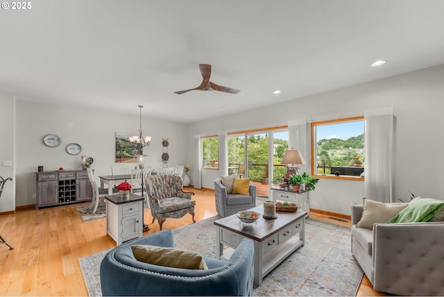 living area featuring light wood finished floors, recessed lighting, baseboards, and ceiling fan with notable chandelier