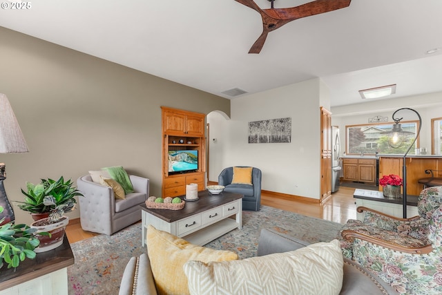 living area featuring arched walkways, light wood-type flooring, ceiling fan, baseboards, and visible vents