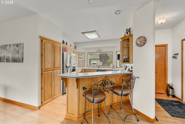 kitchen featuring a breakfast bar area, a peninsula, light wood-type flooring, and baseboards