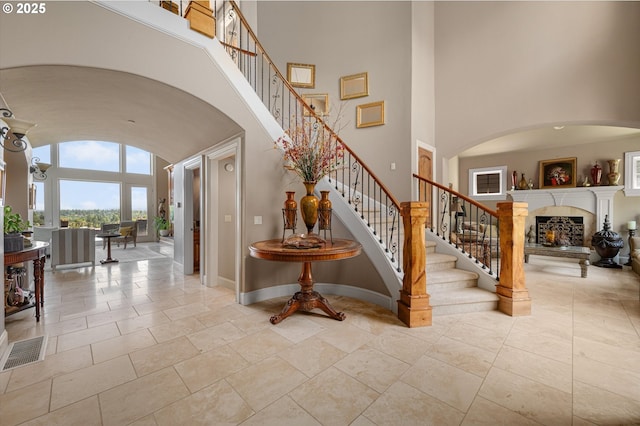 2650 Lorinda Ln, West Linn, OR 97068 - staircase with a lit fireplace, arched walkways, a high ceiling, baseboards, and stone tile flooring