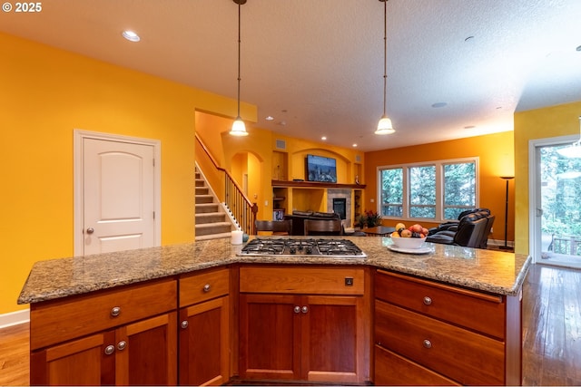kitchen with open floor plan, a tiled fireplace, wood finished floors, and stainless steel gas stovetop
