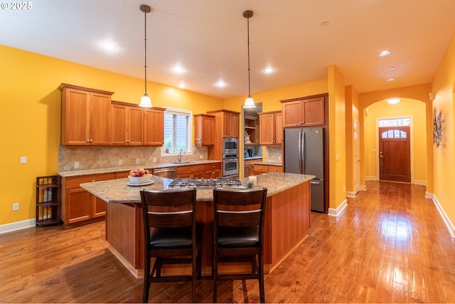 kitchen with stainless steel appliances, light wood finished floors, brown cabinetry, and a sink