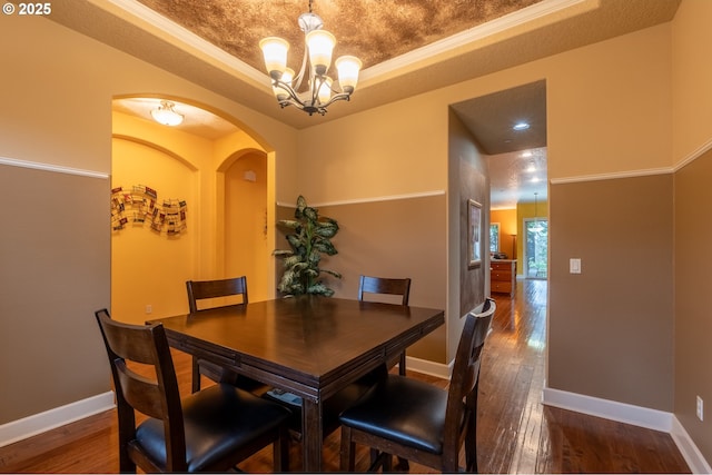 dining area with baseboards, a raised ceiling, arched walkways, a notable chandelier, and dark wood-type flooring