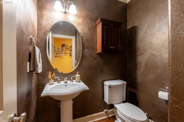 half bathroom with toilet, wood finished floors, and baseboards