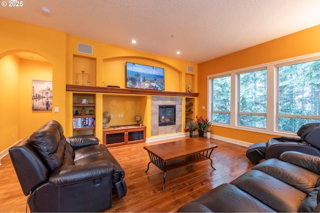 living area with visible vents, built in features, baseboards, hardwood / wood-style flooring, and a textured ceiling