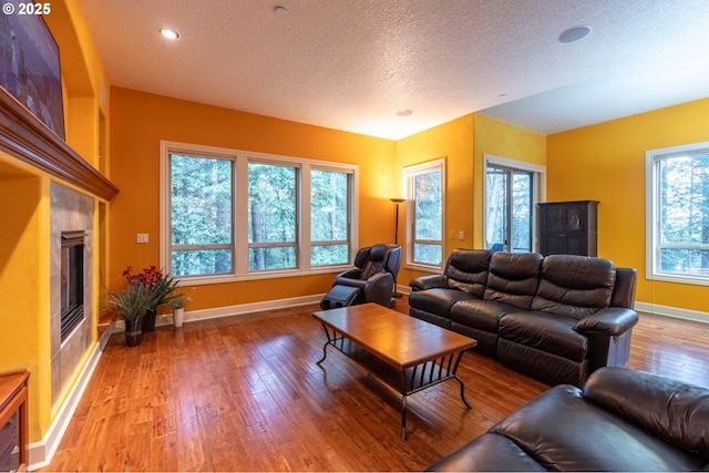 living area featuring baseboards, a wealth of natural light, a fireplace, a textured ceiling, and hardwood / wood-style floors